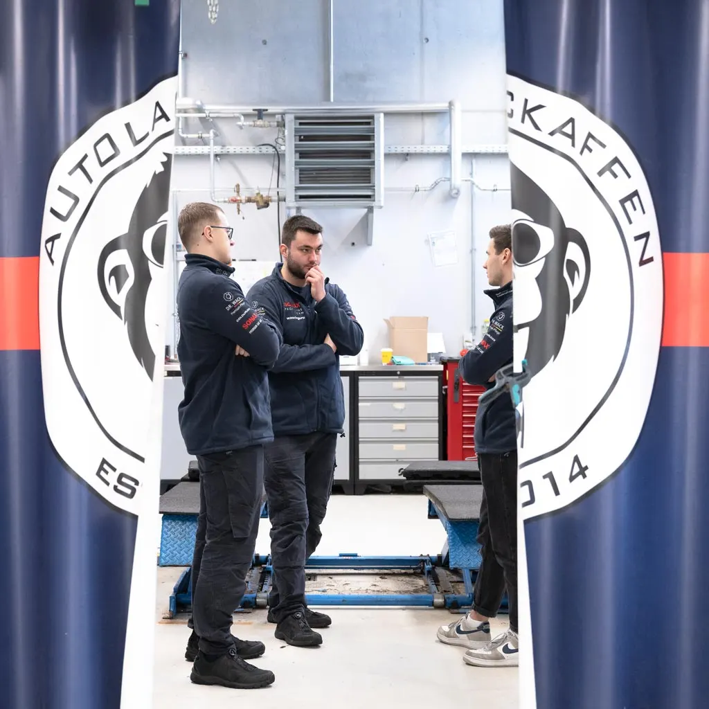 Drei Mitarbeiter vor der Logo-Wand im Detailing-Center