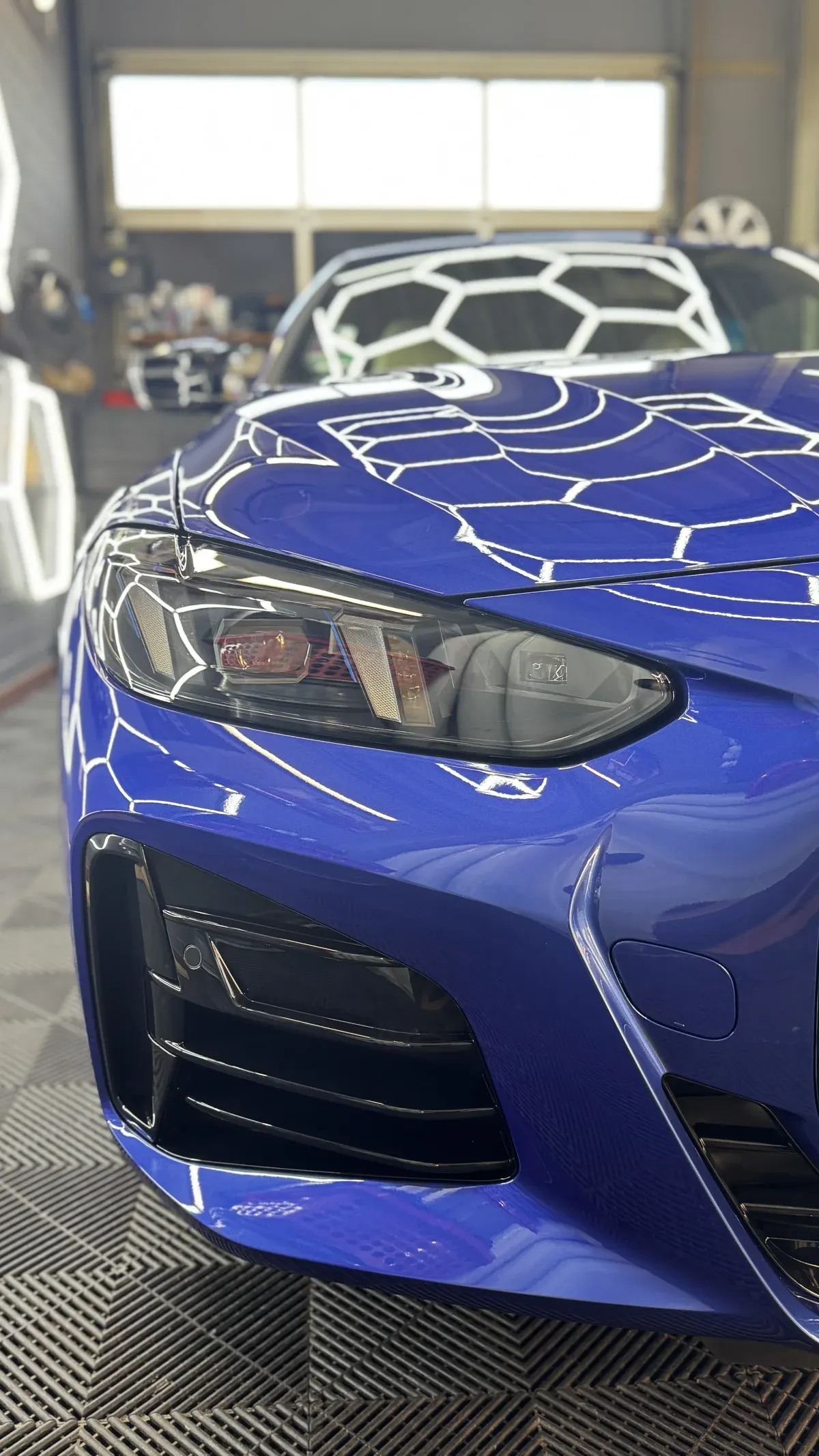 Front eines blauen BMW mit Spiegelungen der Hallenbeleuchtung