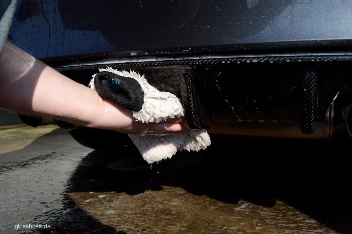 Gloved hand wiping a glossy black rear bumper with a microfiber wash mitt