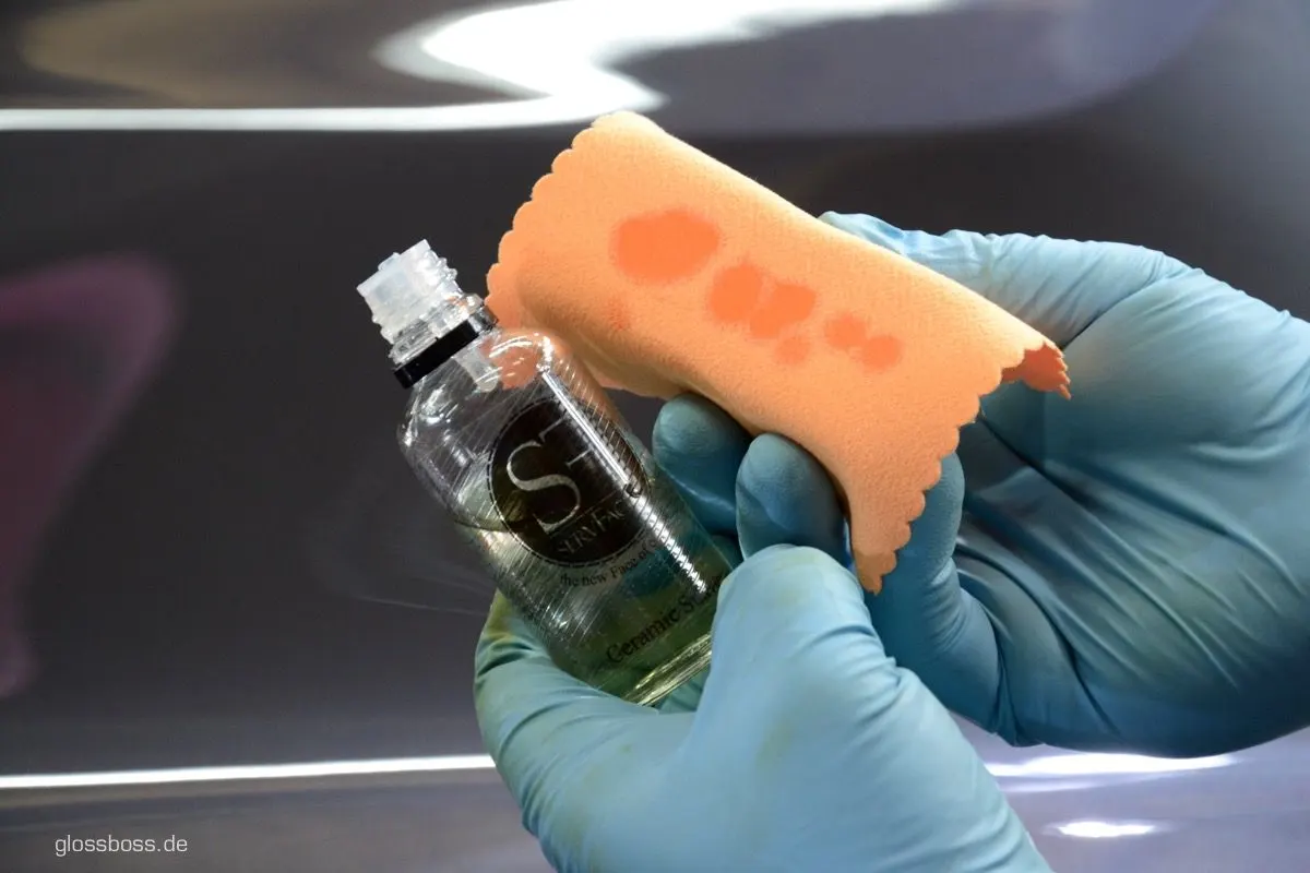 Gloved hands holding a bottle of paint sealant and a foam applicator