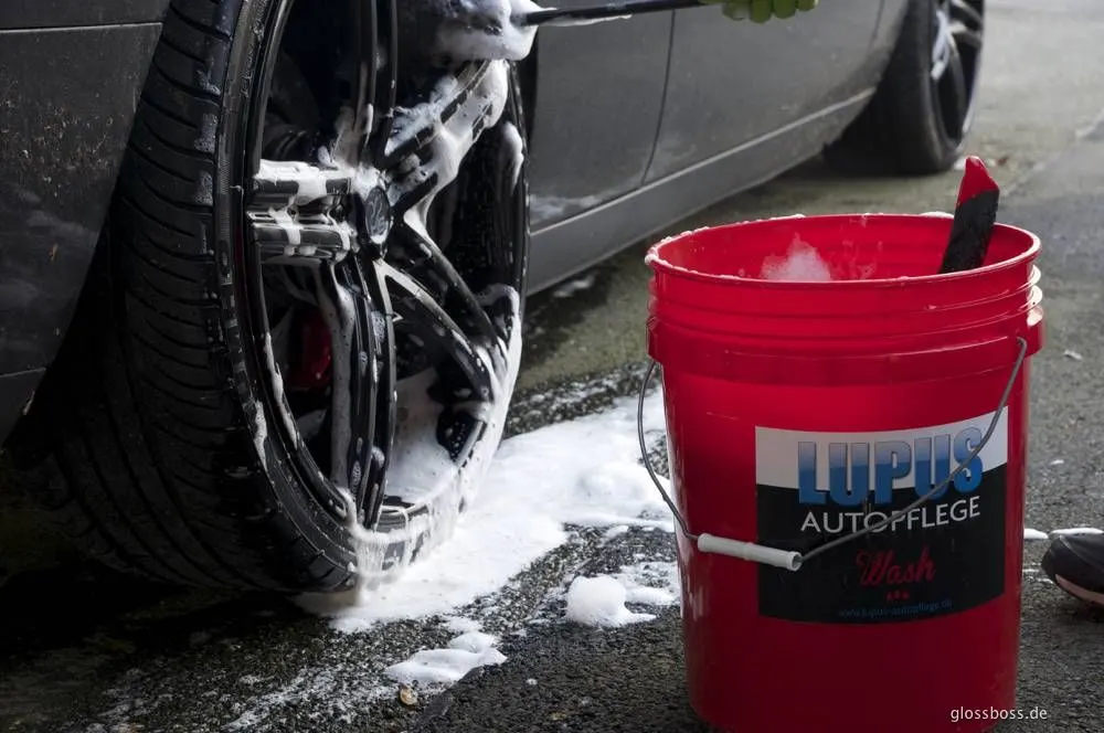 Foamed-up alloy wheel being hand washed next to a red wash bucket