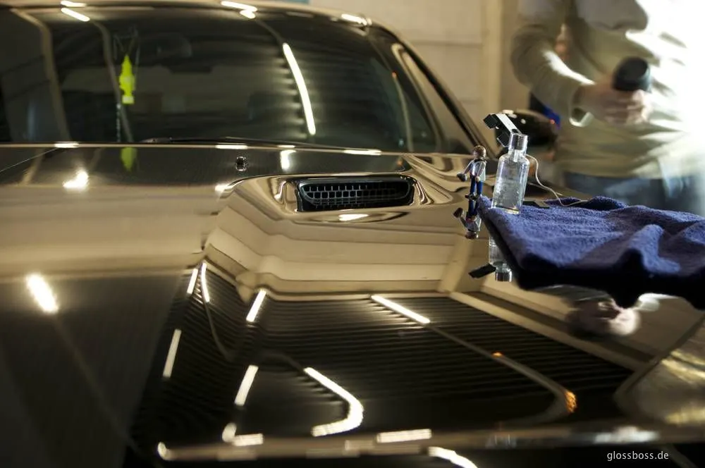 Mirror-finish black Challenger hood reflecting the shop lights, a coating bottle on a towel beside it