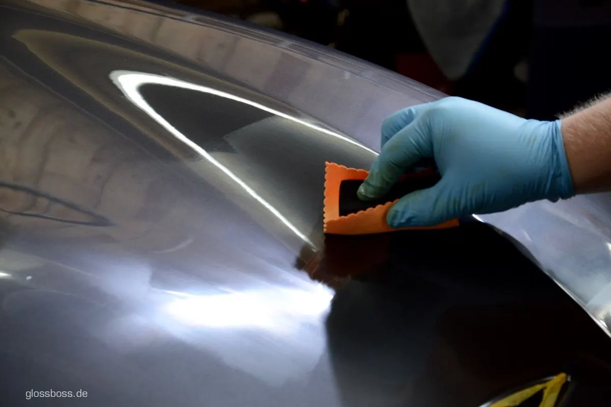 Installer working an orange squeegee across the curve of a grey fender